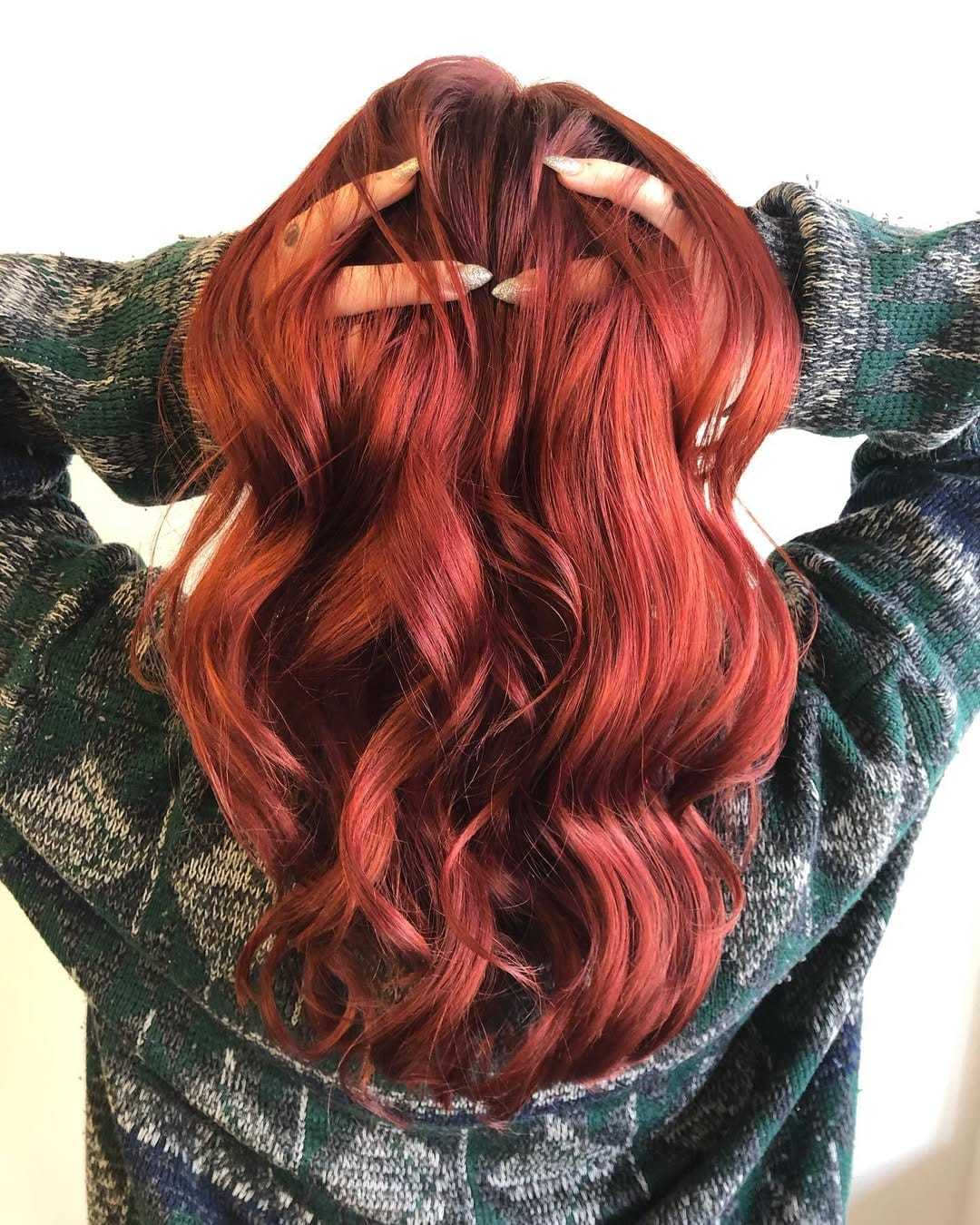Person with long, wavy, red hair, wearing a green and gray plaid sweater, hands in hair.