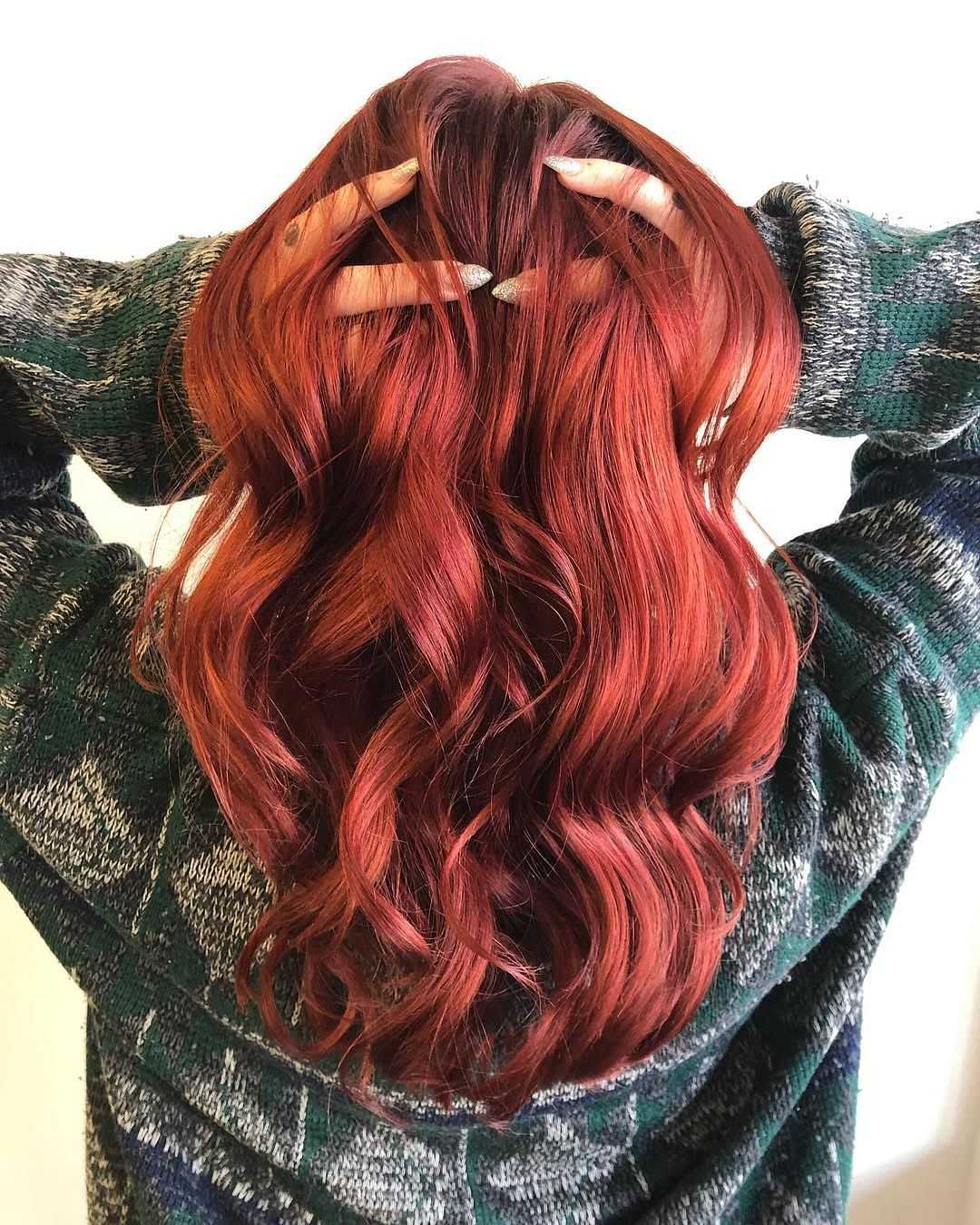 Person with long, wavy, red hair, wearing a green and gray plaid sweater, hands in hair.
